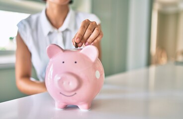 Young brunette woman smiling happy putting money savings inside of piggy bank