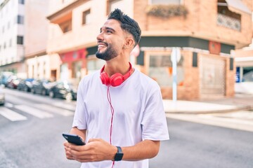 Young arab man smiling happy using smartphone and headphones at the city.