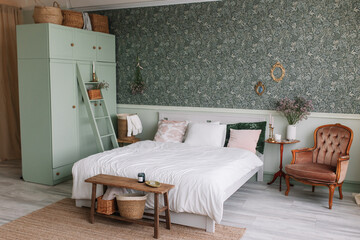 Bedroom in green Scandinavian style Wardrobe with baskets for things Bed with pink and green pillows Table with candles and dried flowers Vintage brown armchair