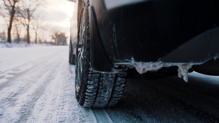 Frozen car driving on the road covered with snow leaving smoke behind. Close up on the wheel. High quality photo