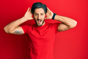 Young hispanic man wearing casual red t shirt smiling cheerful playing peek a boo with hands showing face. surprised and exited