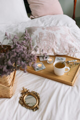 Tray with a mug of tea and candles on the bed Basket with dried flowers near mirror