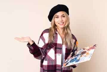 Teenager artist girl holding a palette isolated on blue background holding copyspace imaginary on...