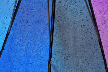 Regenschirm von innen mit blauer, lila und grauer Fläche, Regentropfen sind sichtbar