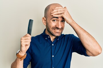 Young hispanic man holding comb loosing hair stressed and frustrated with hand on head, surprised and angry face
