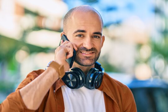 Young hispanic bald man smiling happy talking on the smartphone using headphones at the city.