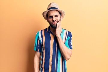 Young handsome man with beard wearing summer hat and shirt touching mouth with hand with painful expression because of toothache or dental illness on teeth. dentist