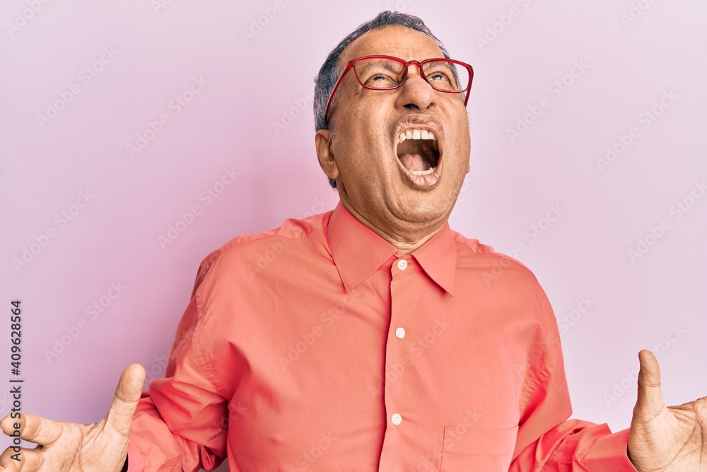 Poster middle age indian man wearing casual clothes and glasses crazy and mad shouting and yelling with agg