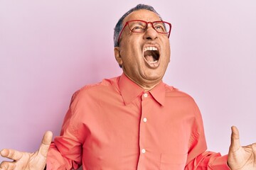 Obraz premium Middle age indian man wearing casual clothes and glasses crazy and mad shouting and yelling with aggressive expression and arms raised. frustration concept.