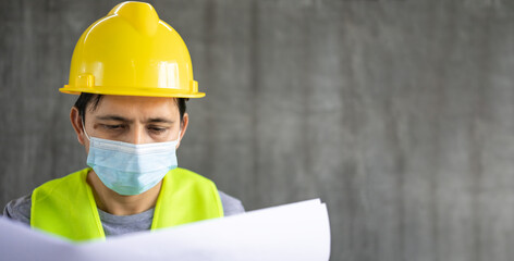 Young asian engineer reading a drawing on cement wall background with copy space