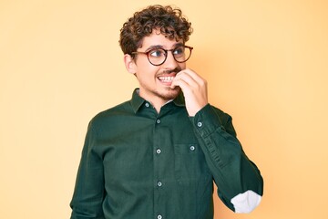 Young caucasian man with curly hair wearing casual clothes and glasses looking stressed and nervous with hands on mouth biting nails. anxiety problem.