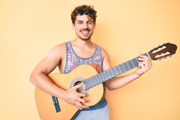 Young caucasian man with curly hair playing classical guitar winking looking at the camera with...