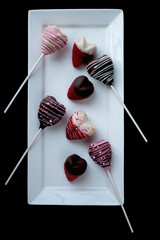 Heart Shape Strawberry Covered Chocolate Pops on White Plate on Black Background.