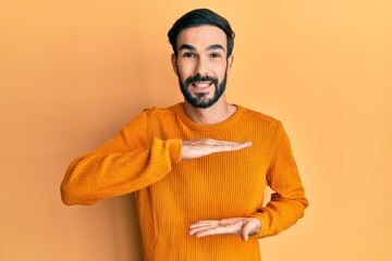 Young hispanic man wearing casual clothes gesturing with hands showing big and large size sign, measure symbol. smiling looking at the camera. measuring concept.