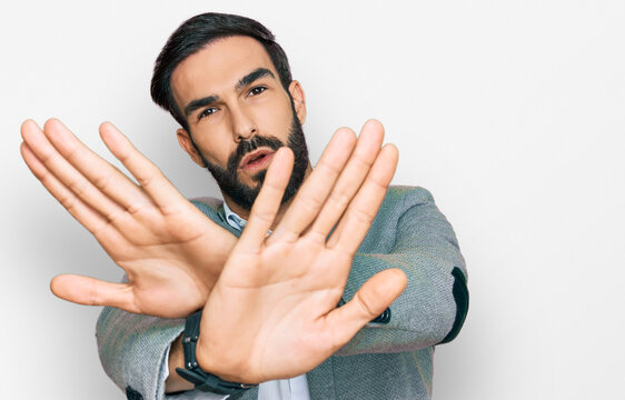 Young hispanic man wearing business clothes rejection expression crossing arms and palms doing negative sign, angry face