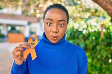Young african american woman with relaxed expression holding orange awareness ribbon at the park.