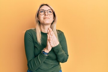 Young caucasian woman wearing casual clothes and glasses begging and praying with hands together...