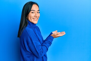 Young asian woman wearing casual winter sweater pointing aside with hands open palms showing copy space, presenting advertisement smiling excited happy