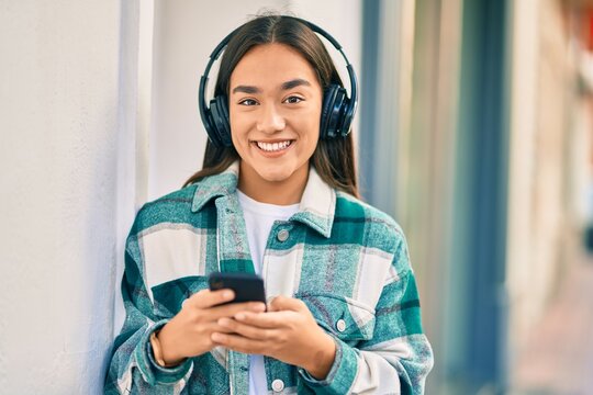 Young latin girl smiling happy using smartphone and headphones at the city.