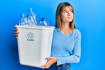 Teenager caucasian girl holding recycling bag with plastic bottles smiling looking to the side and staring away thinking. - obrazy, fototapety, plakaty