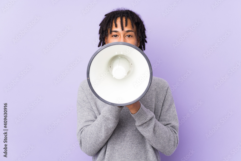 Sticker Young african american man isolated on purple background shouting through a megaphone