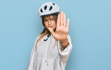 Teenager caucasian girl wearing bike helmet doing stop sing with palm of the hand. warning expression with negative and serious gesture on the face.