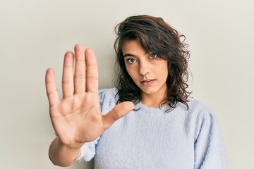 Young hispanic woman wearing casual winter sweater doing stop sing with palm of the hand. warning...