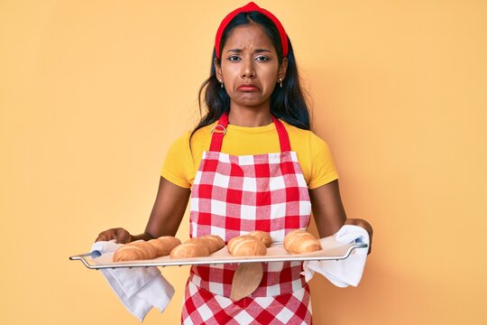 Young indian girl wearing baker uniform holding homemade bread depressed and worry for distress, crying angry and afraid. sad expression.