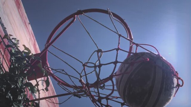 Upward view, a basketball ball hits the basket in the sports yard. The player successfully throws the ball into the hoop, scores a point, a three-point goal. Street and sports motivation. Slow motion