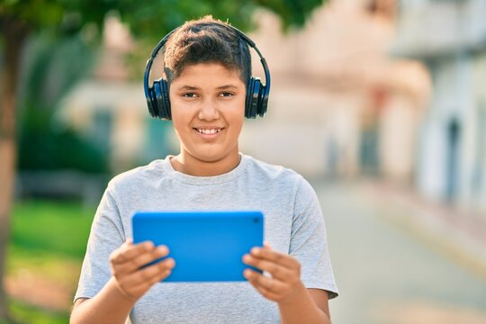 Adorable latin boy smiling happy using headphones and touchpad at the park.