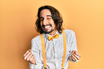 Young hispanic man wearing hipster elegant look very happy and excited doing winner gesture with...