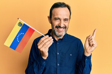 Middle age hispanic man holding venezuelan flag smiling happy pointing with hand and finger to the side
