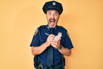 Middle age hispanic man wearing police uniform writing traffic fine celebrating crazy and amazed...