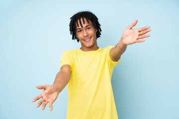 Young african american man isolated on blue background presenting and inviting to come with hand