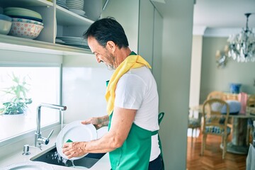 Fototapeta premium Middle age man with beard smiling happy washing dishes at home