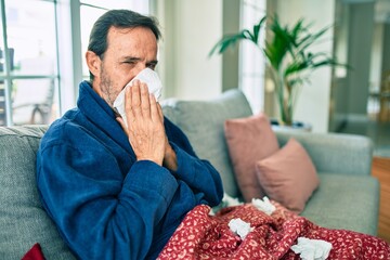 Middle age man feeling sick with cold and fever at home, ill with flu disease sitting on the sofa