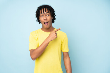Young african american man isolated on blue background surprised and pointing side