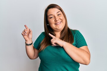 Beautiful brunette plus size woman wearing casual clothes smiling and looking at the camera pointing with two hands and fingers to the side.