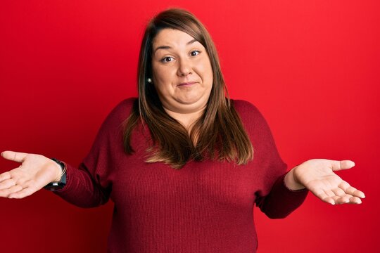 Beautiful brunette plus size woman wearing casual clothes clueless and confused expression with arms and hands raised. doubt concept.