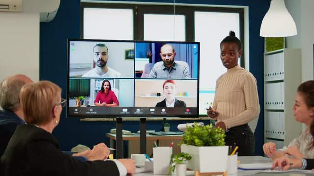 Black manager woman talking with remotely colleagues on video call at tv screen, presenting new business partners. Confident businesswoman talking to web cam streaming webcast training, doing online