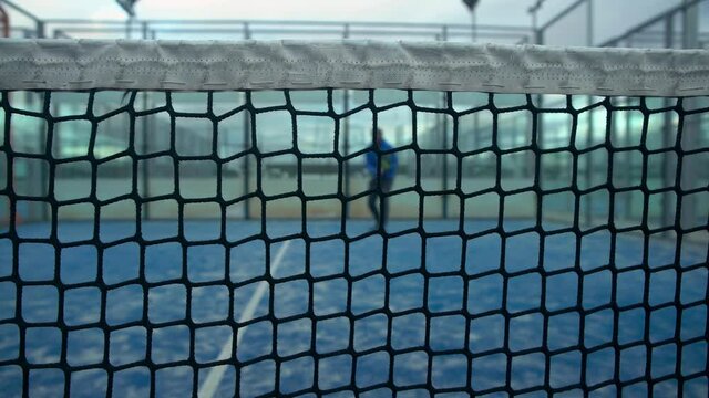 Through grid view of paddle tennis man playing on blue court outdoors. One caucasian padle player sportman hitting the ball. Racquet sport game Concept.-Dan
