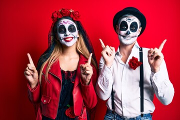 Couple wearing day of the dead costume over red smiling confident pointing with fingers to...