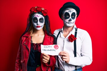 Couple wearing day of the dead costume holding happy halloween paper relaxed with serious expression on face. simple and natural looking at the camera.