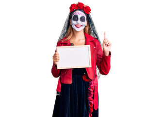Woman wearing day of the dead costume holding empty white chalkboard surprised with an idea or question pointing finger with happy face, number one