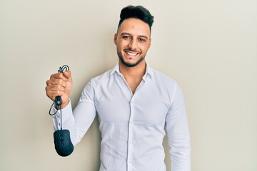 Young arab man holding computer mouse device looking positive and happy standing and smiling with a...
