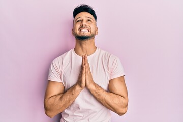 Young arab man wearing casual clothes begging and praying with hands together with hope expression...