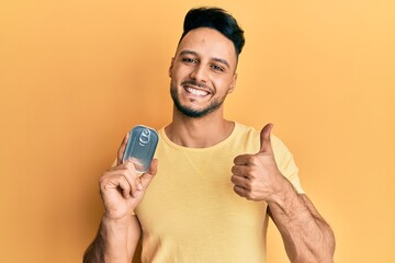 Young arab man holding canned food smiling happy and positive, thumb up doing excellent and approval sign