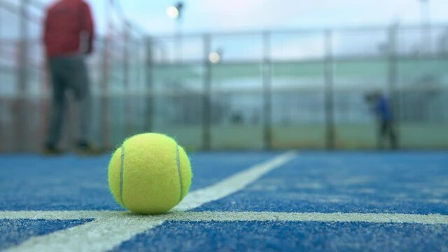 Yellow ball on floor behind padel net in blue court outdoors. Man who playing paddle tennis. One caucasian player sportman hitting balls. Racquet sport game Concept.-Dan