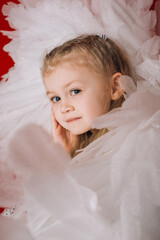 little girl 4 years old in white angel wings on a red latex background in the studio for valentine's day