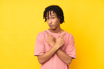 Young african american man isolated on yellow background pointing to the laterals having doubts